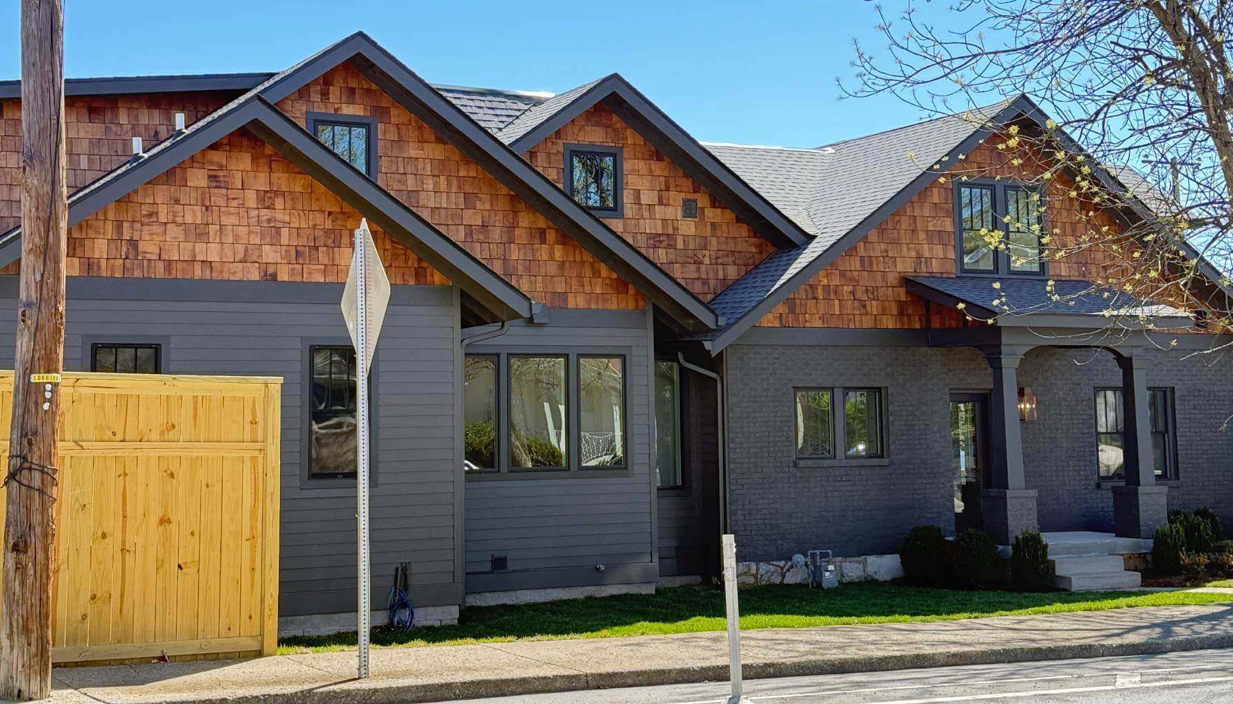 A modern house with gray siding and wooden shingles on a sunny day.
